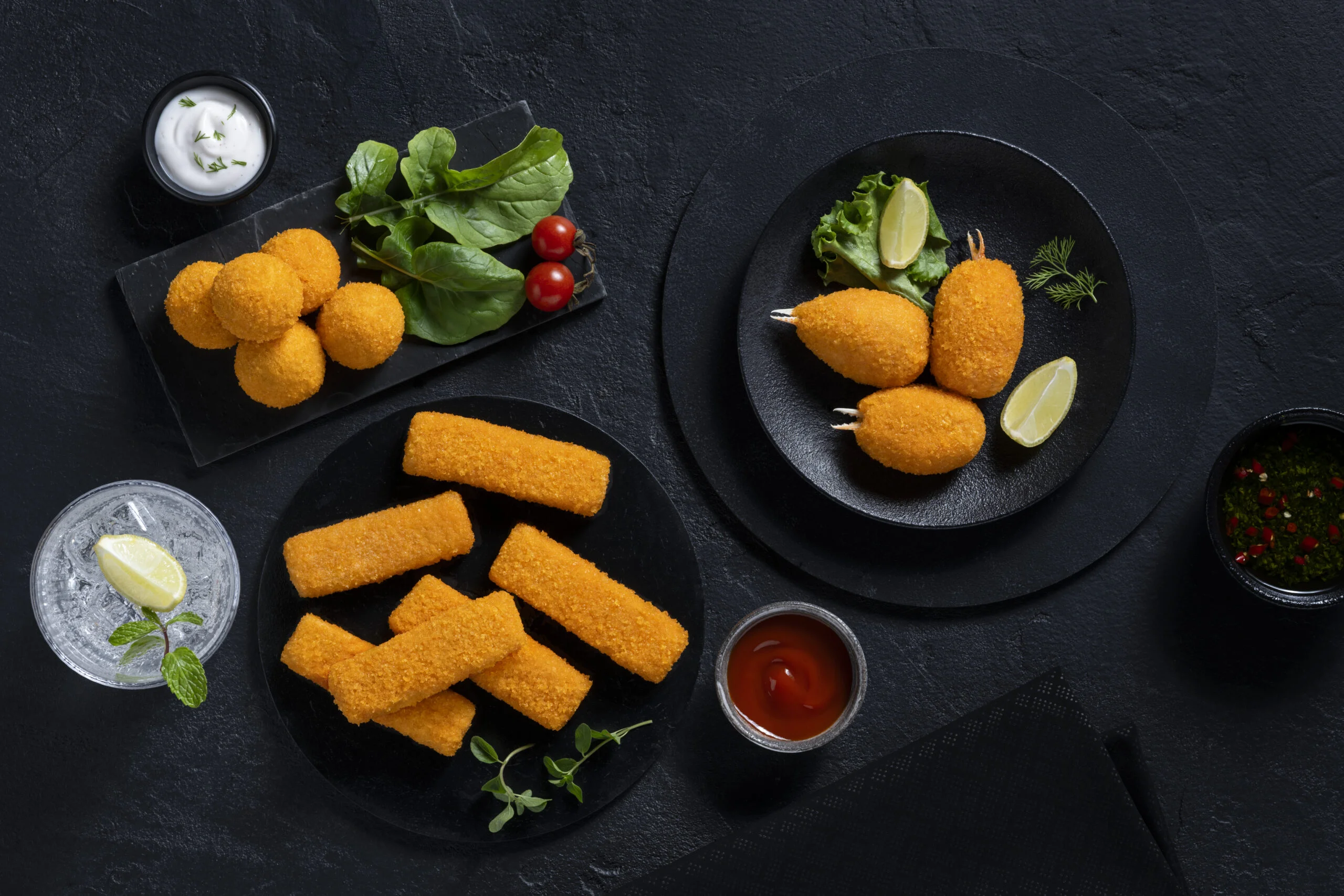 Assorted crispy fried seafood snacks served with dips on black plates.