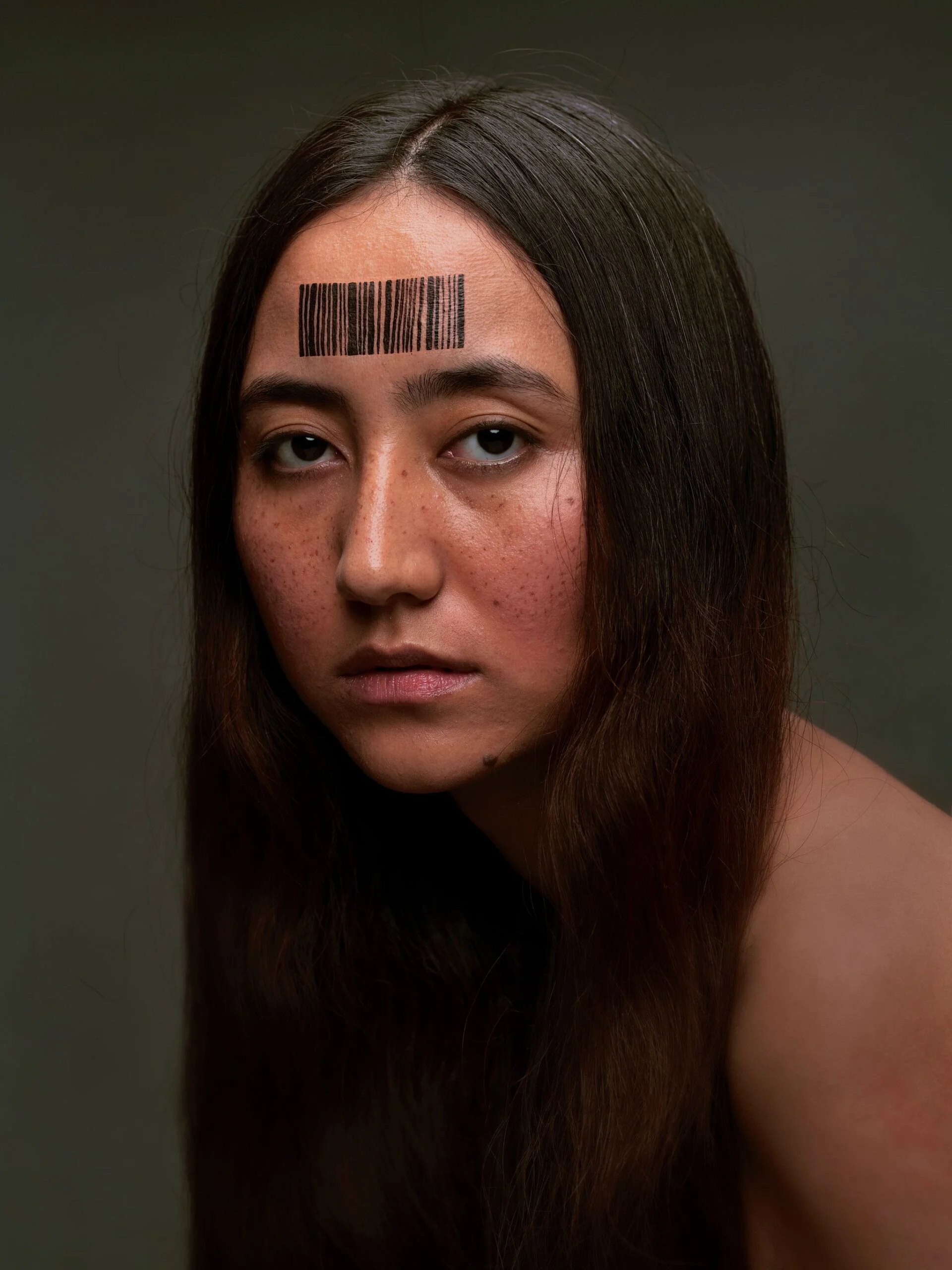 Portrait of a woman with long hair and a black barcode painted on her forehead.