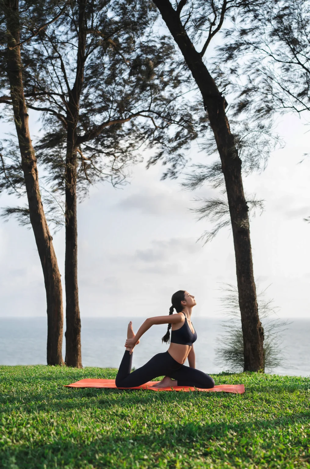 Woman practicing yoga on a grassy seaside hill.