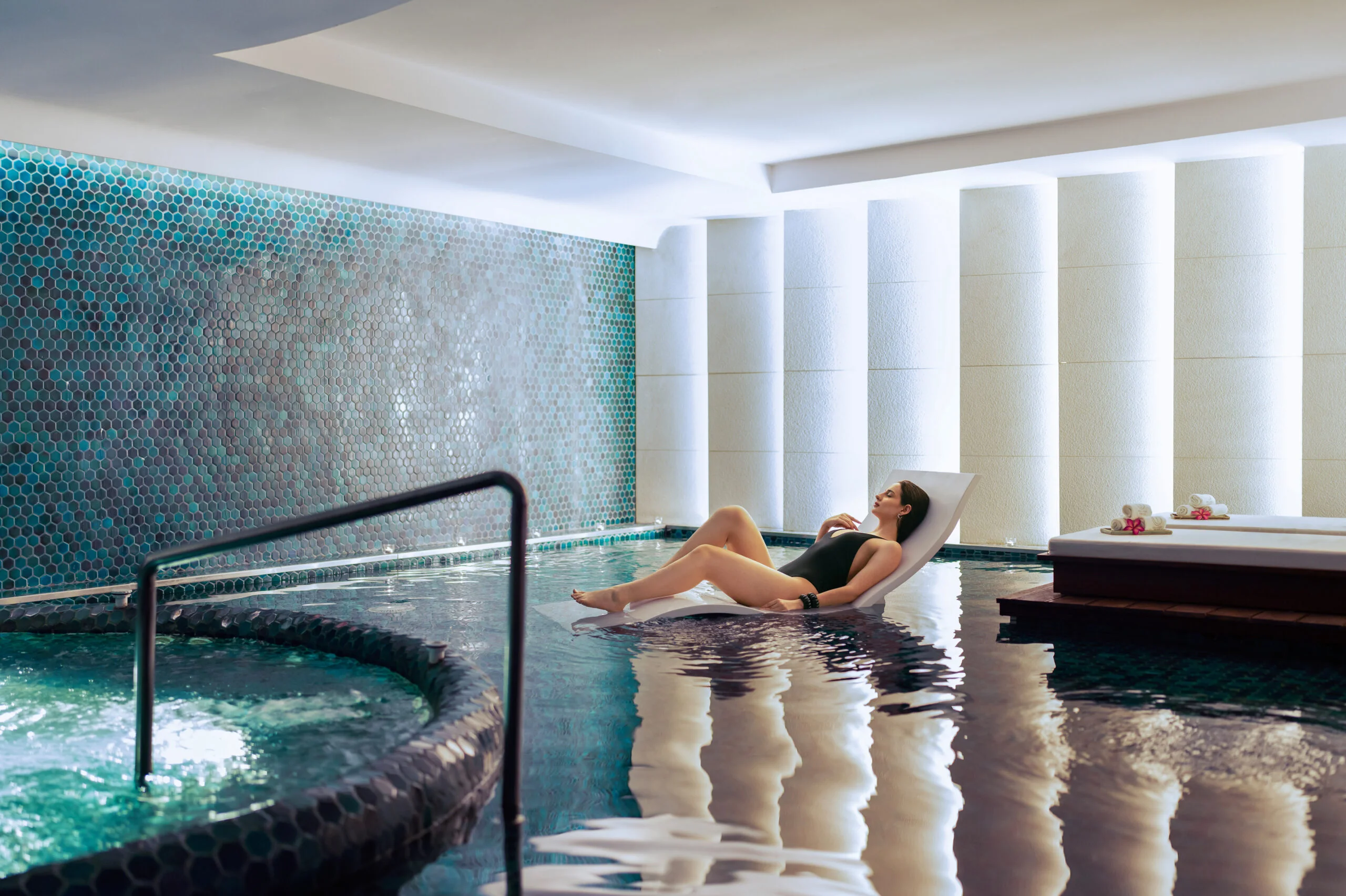 Woman relaxing on a pool lounger at an indoor spa.