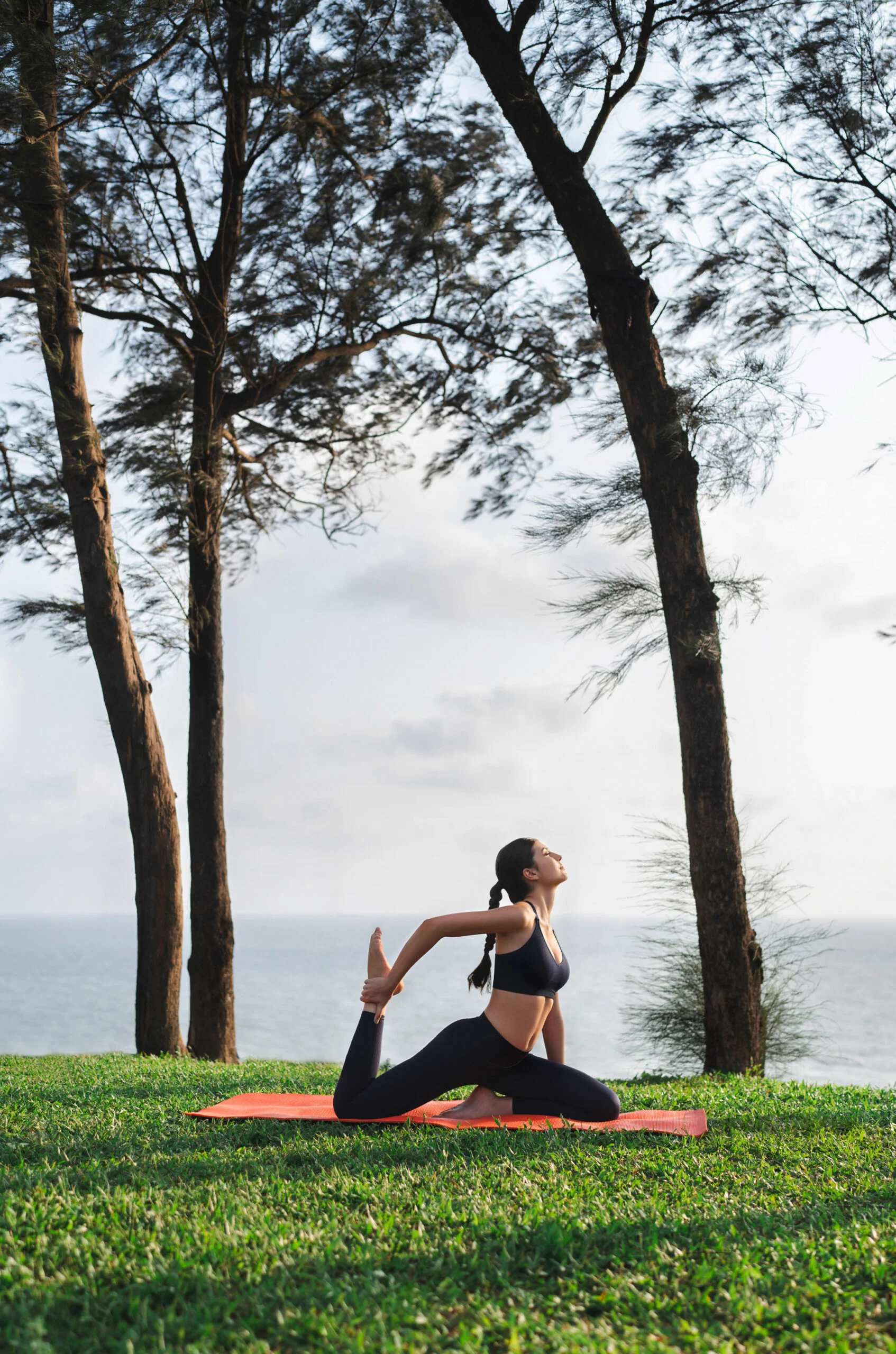 Woman practicing yoga on a grassy seaside hill.