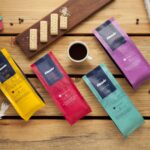Colorful premium coffee packs styled with snacks, chocolate, and a fresh cup of brew.
