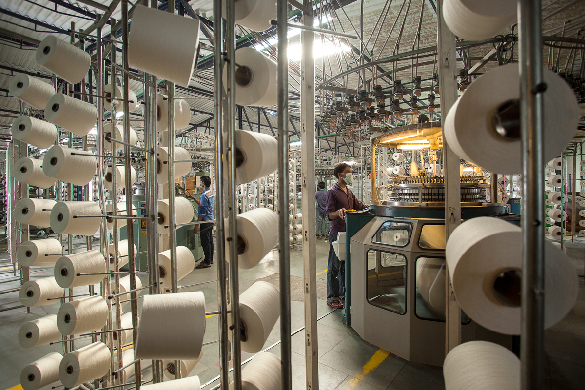 Textile factory with yarn spools and automated knitting machines in operation.