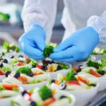 Gloved hands preparing fresh salad bowls.