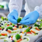 Gloved hands preparing fresh salad bowls.