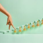 Hand reaching toward gold earrings arranged on pastel steps.