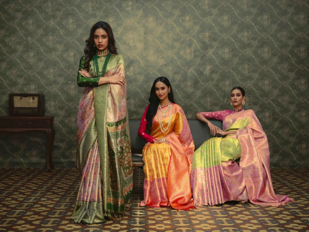 Three women in green, orange and pink Kanjivaram silk sarees in a vintage-styled living room set for a Seematti festive campaign